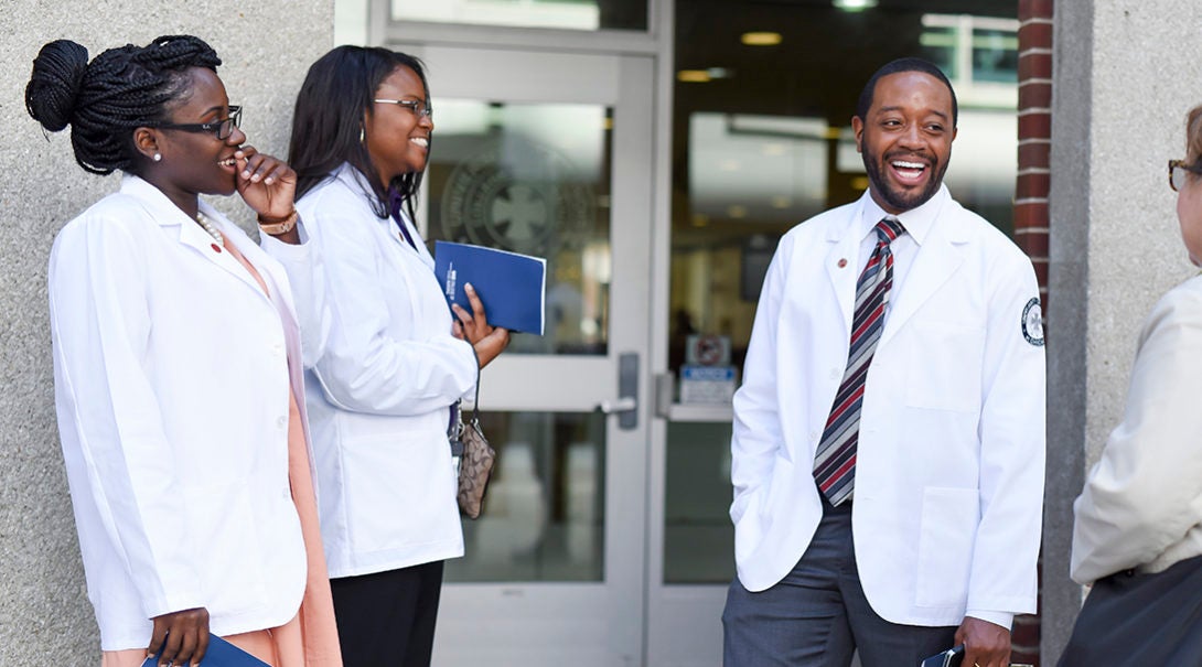 Three Black medical professionals talking in front of a doorway