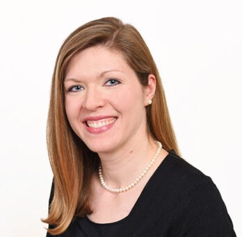 Woman with dark blonde hair, a pearl necklace and black shirt smiles at camera 