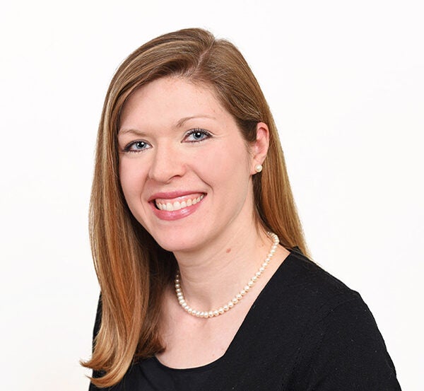 Woman with dark blonde hair, a pearl necklace and black shirt smiles at camera