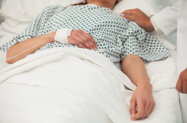 Woman in hospital bed with nurses hand on shoulder