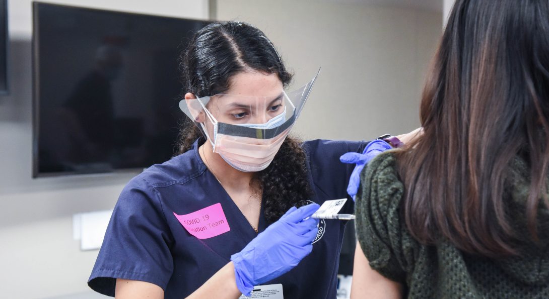 Student Jasmine Medina administers vaccine to a woman whose face is not visible