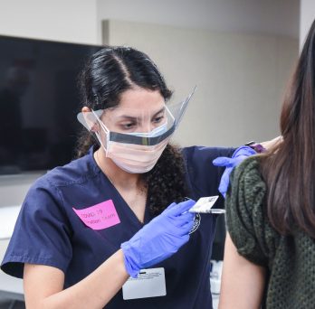 Student Jasmine Medina administers vaccine to a woman whose face is not visible
                  
