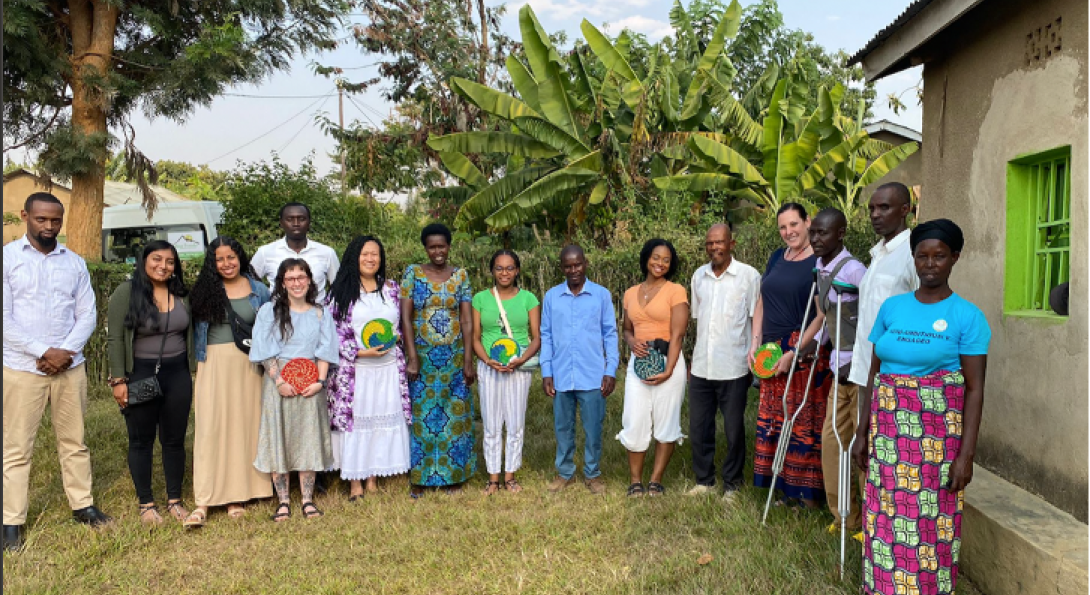 Group of people standing in a semi-circle outdoors next to building and with trees in the background.