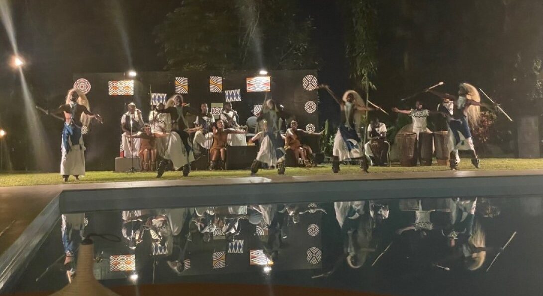 Traditional Rwandan dancers and musicians perform outdoors next to a pool.