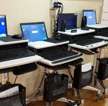 Row of laptops on rolling carts with screen showing Epic software logo
                  