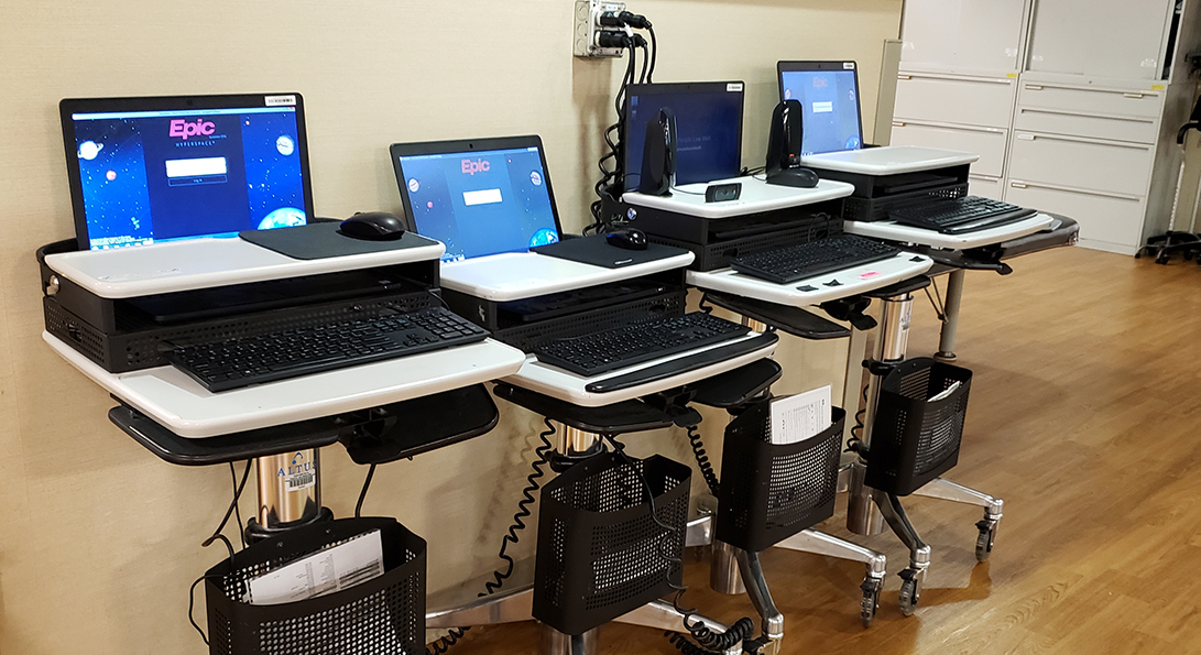 Row of laptops on rolling carts with screen showing Epic software logo