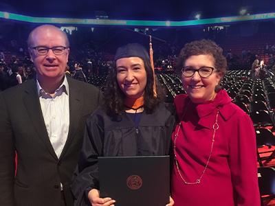 Young woman in cap and gown with parents at graduation ceremony