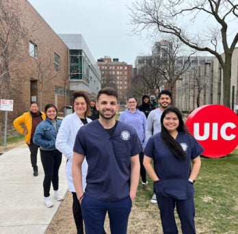 group of students and faculty stand in front of UIC logo 