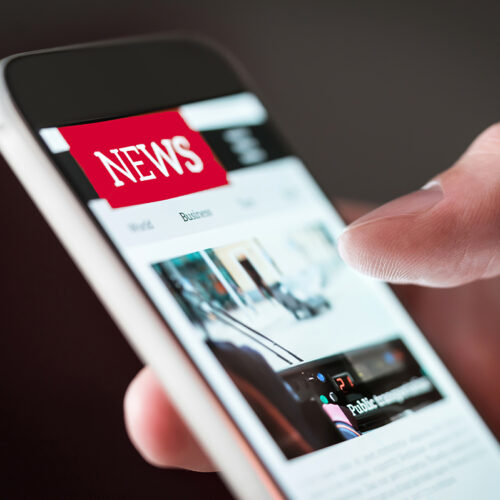 close-up of right hand holding a smartphone and looking at a page titled News