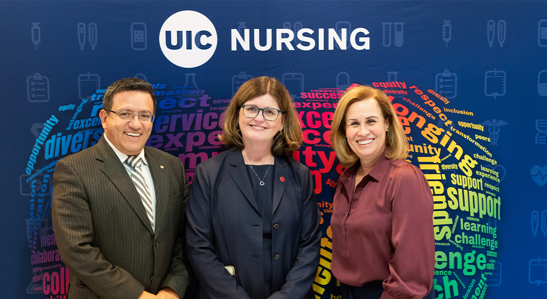 A man, a woman and a second woman post in front of a colorful banner branded for the UIC College of Nursing