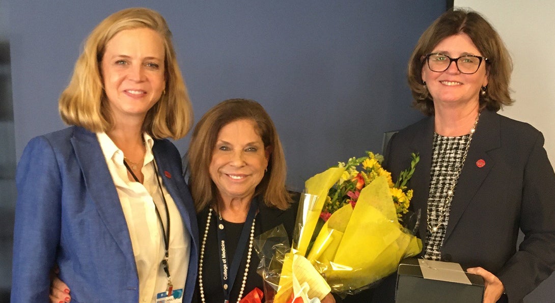 A woman holds a bouquet of flowers and poses with two other women after winning an award