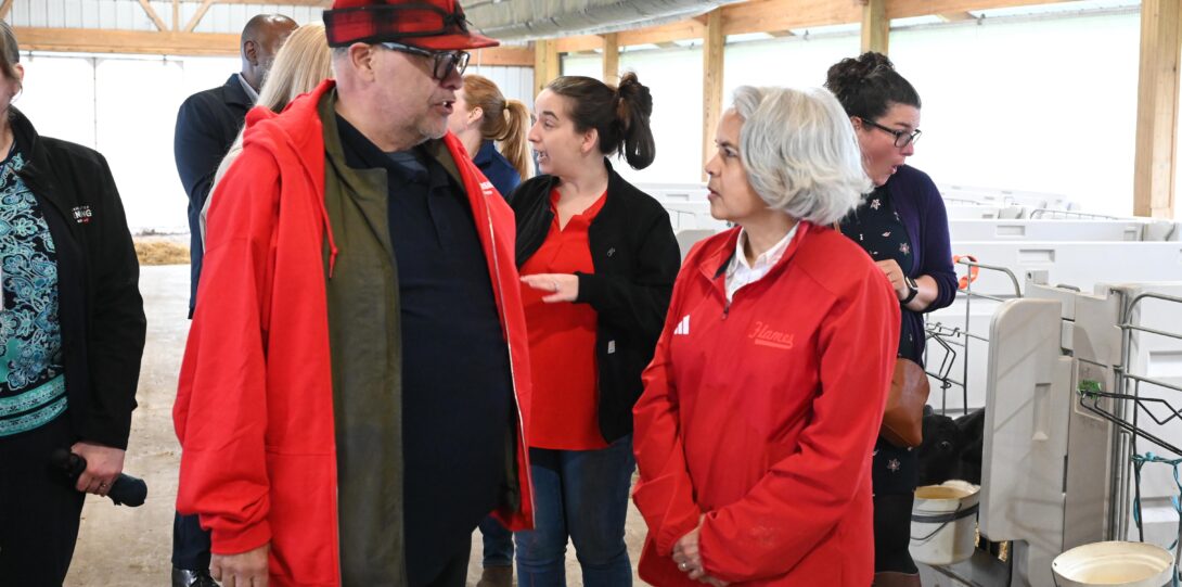 A woman with white hair and a red jacket stands talking to a taller man wearing an open red jacket and a black-and-red cap