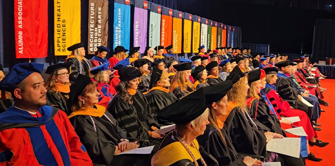 group of robbed academics sit on stage and listen to speaker