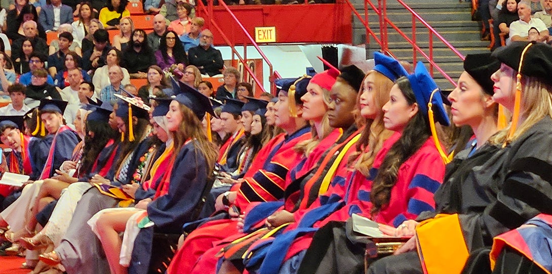 A row of graduating students listen to speaker during ceremony