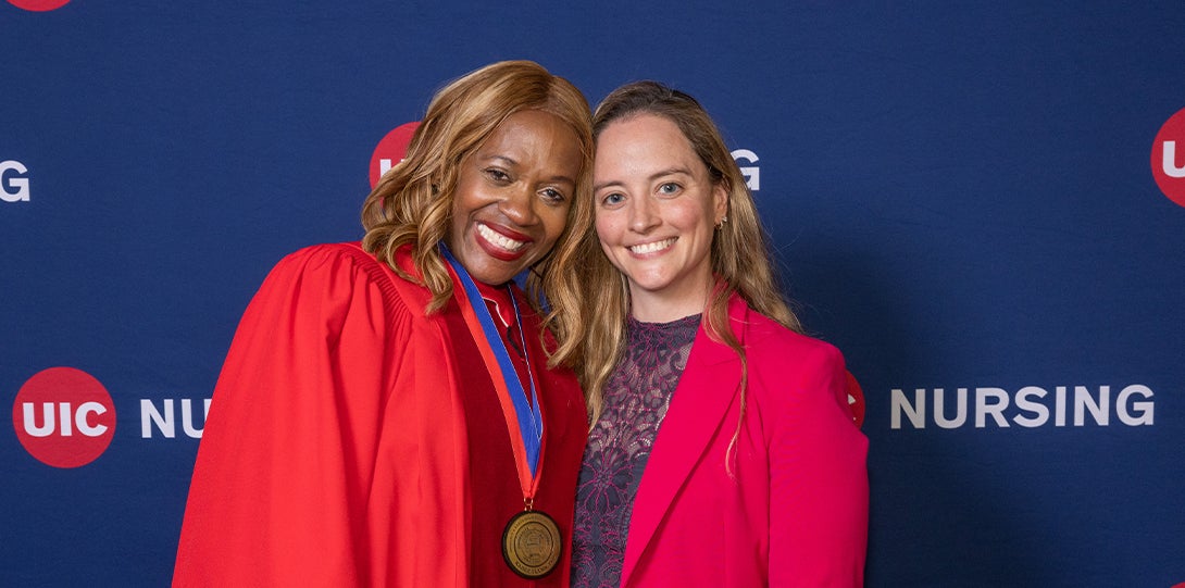 Two women smile for a photo in front of a UIC Nursing banner