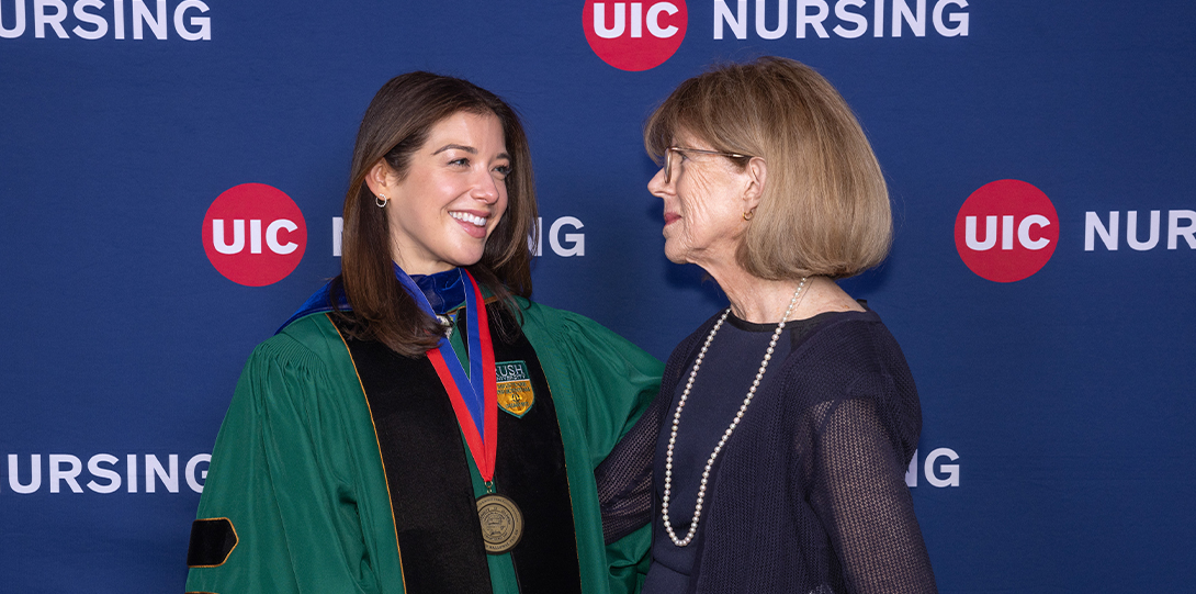 Two women embrace in front of a UIC Nursing banner