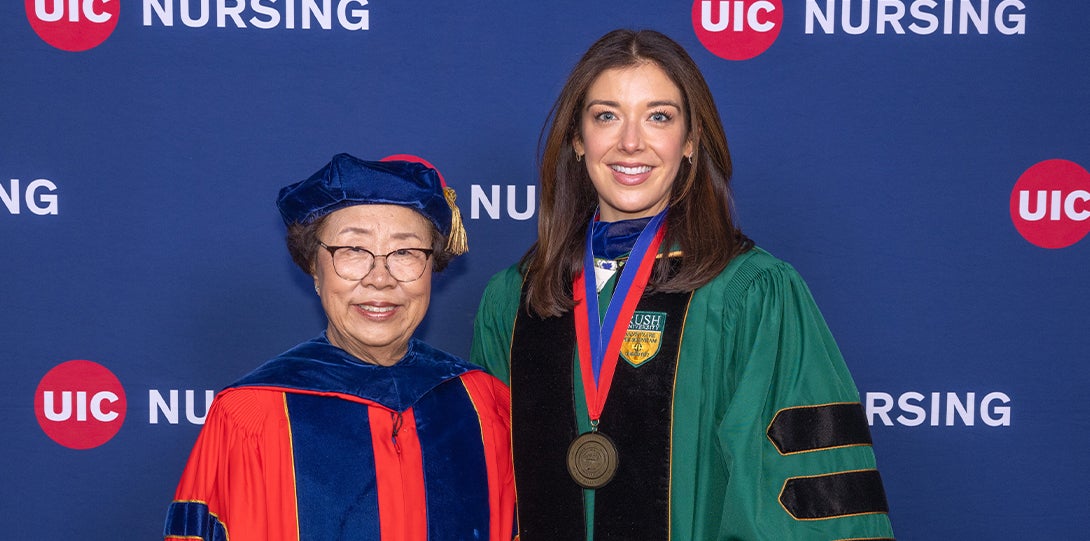 Two women smile for a photo in front of a UIC Nursing banner