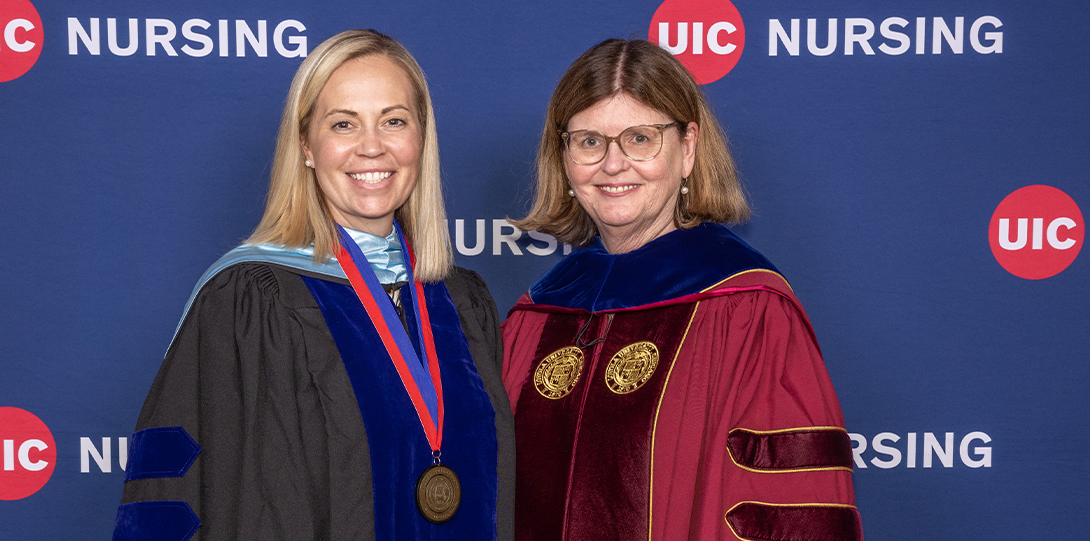 Two women smile for a photo in front of a UIC Nursing banner