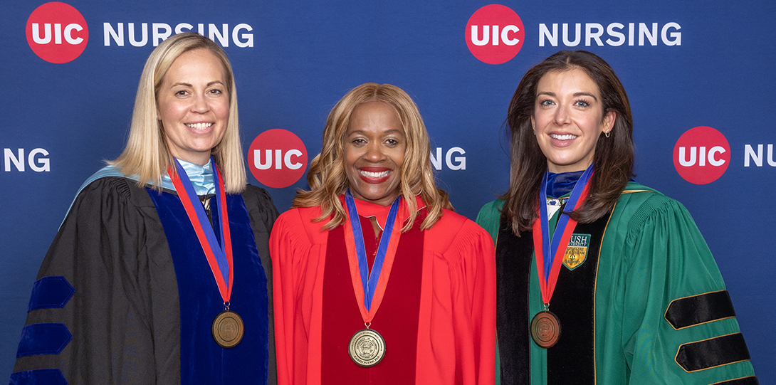 Three women smile for a photo in front of a UIC Nursing banner