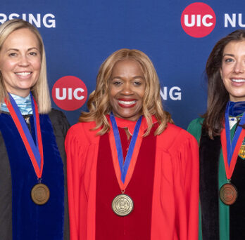Three women pose for picture in front of UIC Nursing banner. 