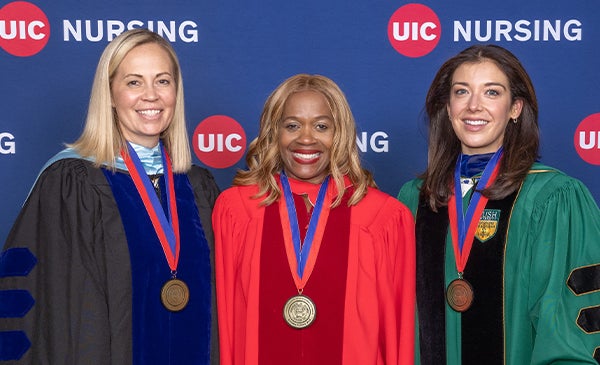 Three women pose for picture in front of UIC Nursing banner.