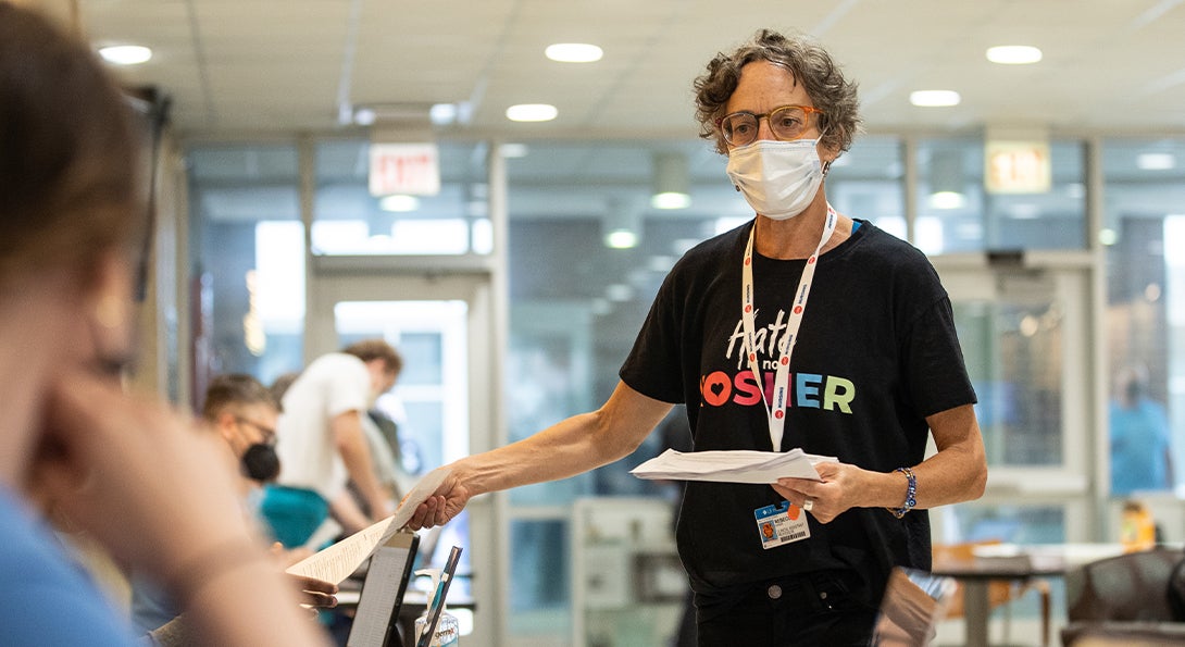 A woman wearing a facemask hands paper to someone off screen.