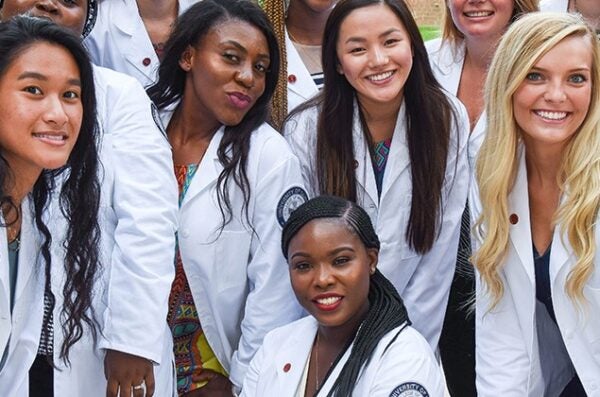 Students wearing white coats crowd together happily to smile at the camera