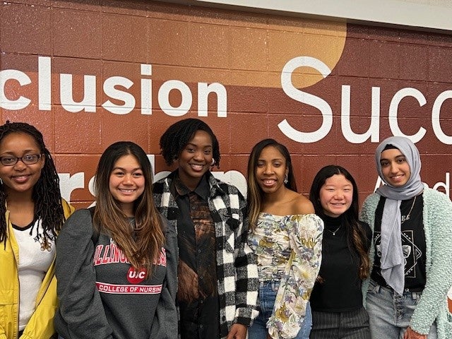 Diverse group of students stand in front of wall with words 