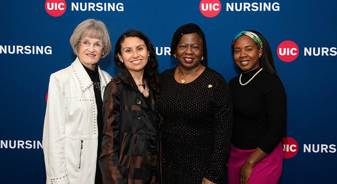 Four women stand side by side to pose for an photo in front of the College of Nursing backdrop