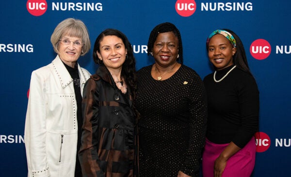 Four women stand side by side to pose for an photo in front of the College of Nursing backdrop