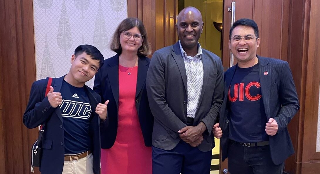 Two men wearing UIC Nursing t-shirts and jackets stand on either side of the UIC Nursing dean and associate dean