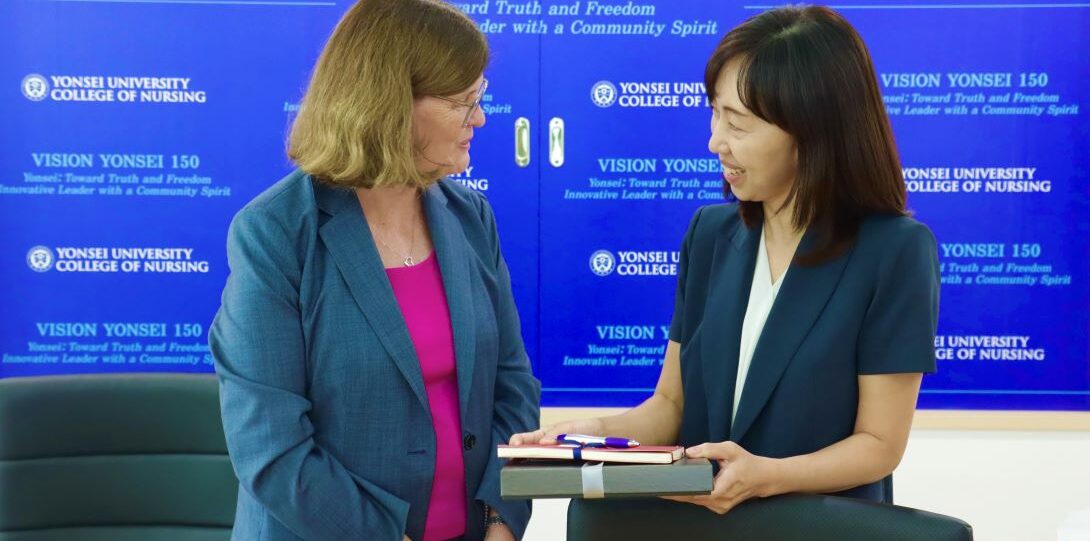 One woman hands another woman a gift in front of Yonsei University board