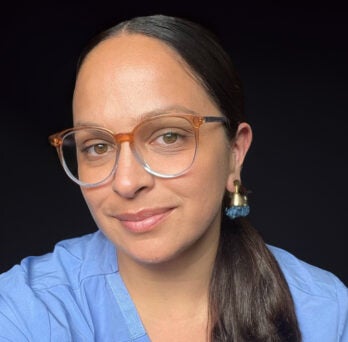 Woman wearing scrubs smiels and looks at camera 