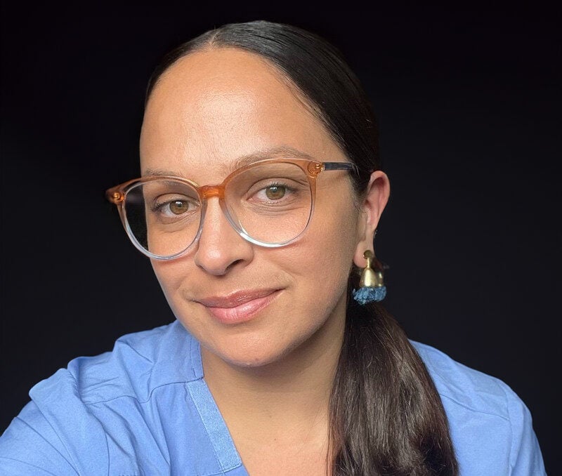 Woman wearing scrubs smiels and looks at camera