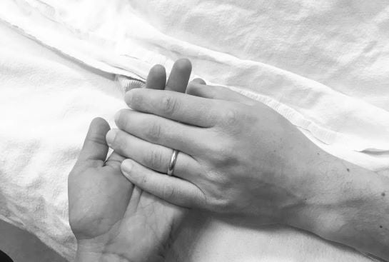 A hand with a wedding ring lays on top of another hand