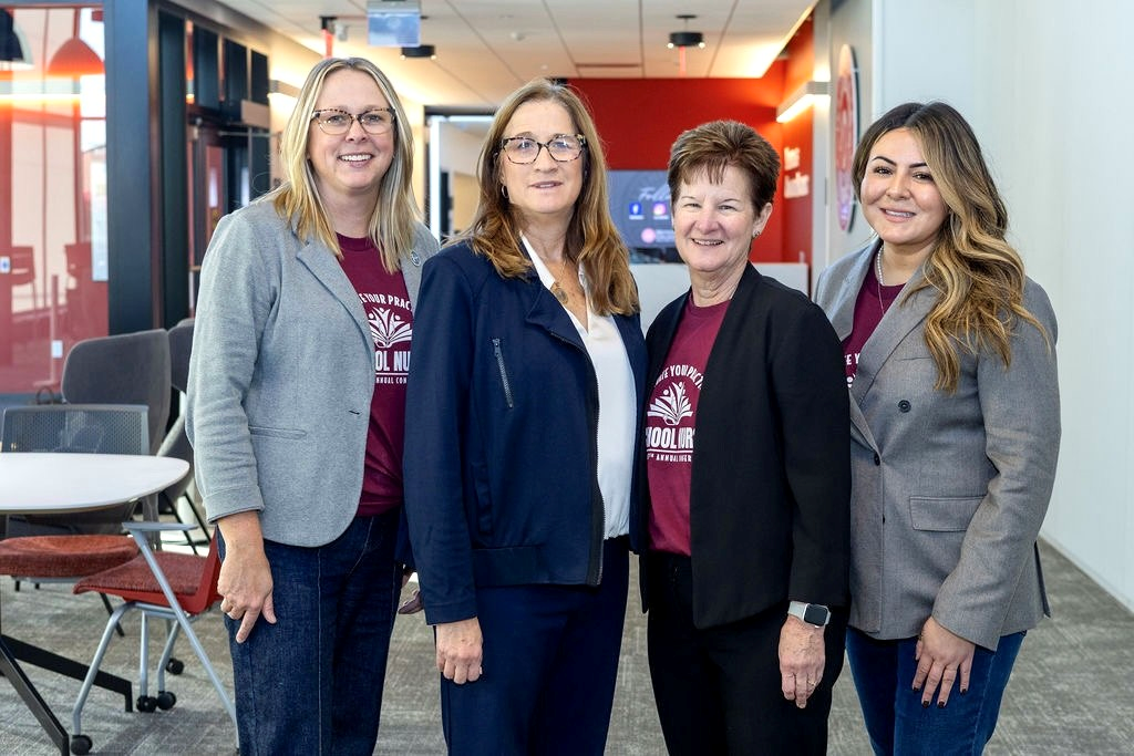 Four women stand next to each other facing the camera wearing blazers