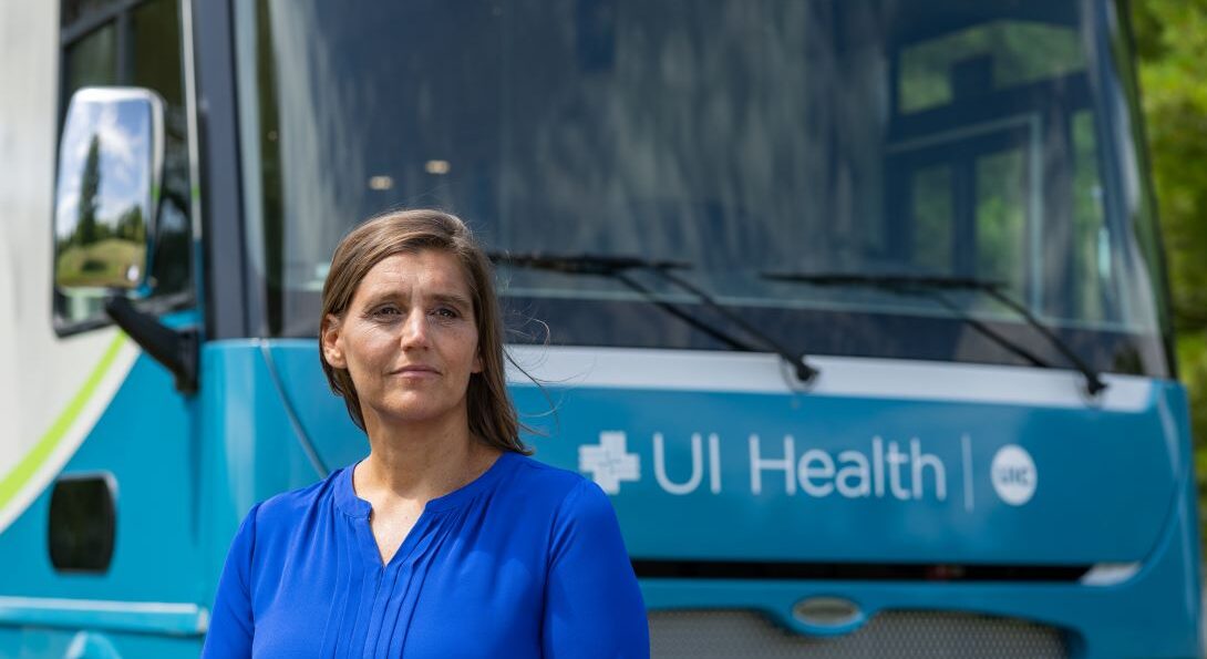 Woman wearing blue blouse stands in front of a van with UI Health written across the front