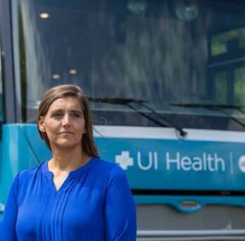 Woman wearing blue blouse stands in front of a van with UI Health written across the front
                  