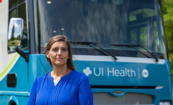 Woman wearing blue blouse stands in front of a van with UI Health written across the front