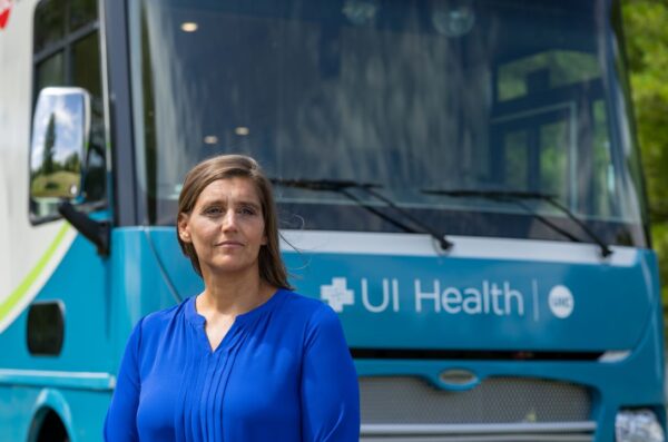 Woman in blue stands in front of coach bus bearing UI Health logo