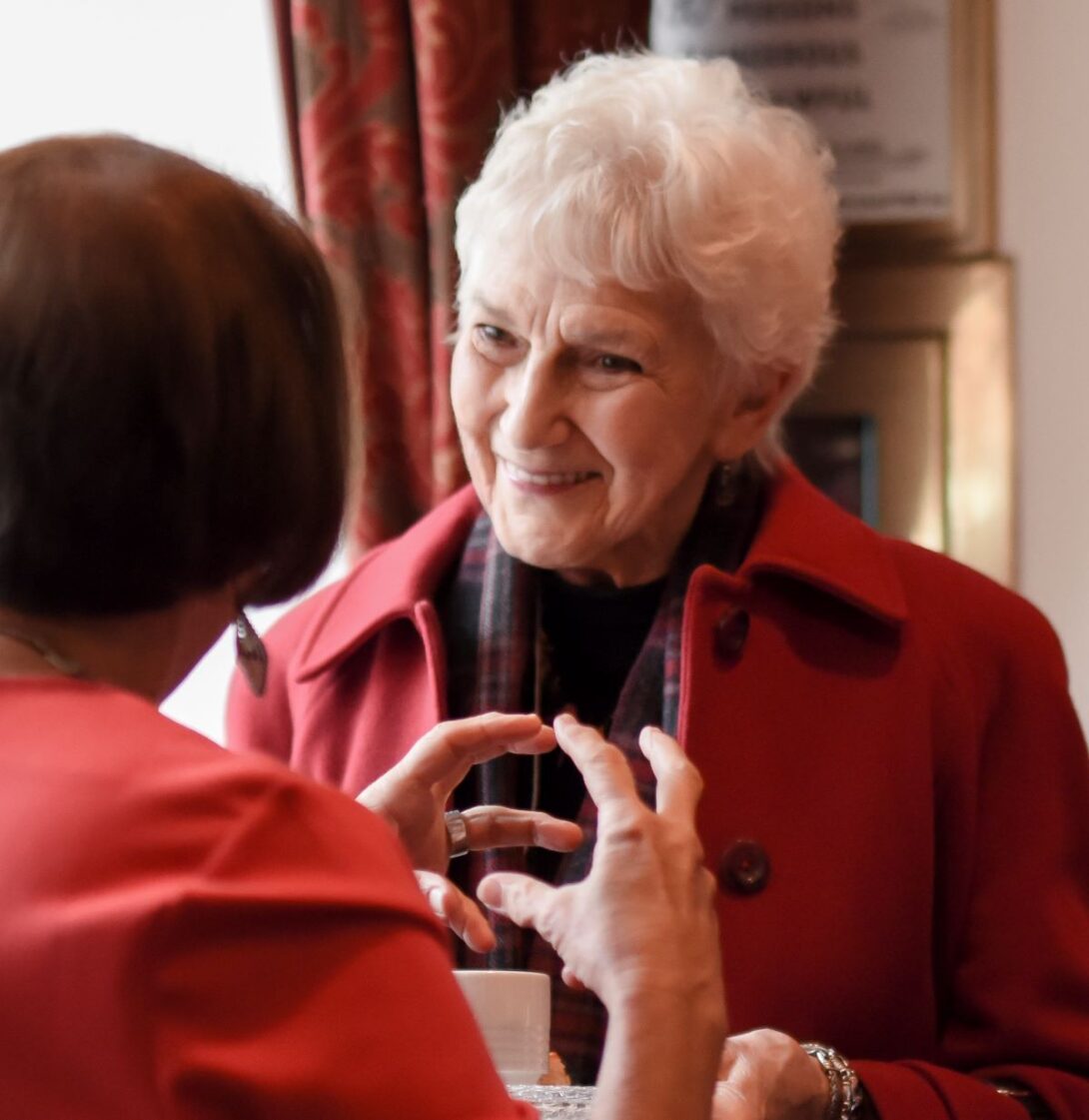 Woman in Red jacket smiles during a conversation with someone not pictured.