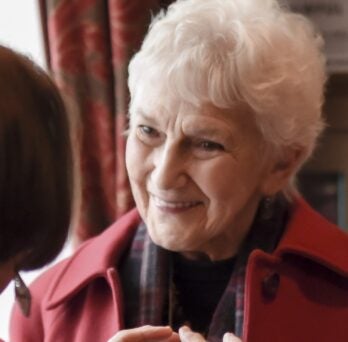 Woman in Red jacket smiles during a conversation with someone not pictured. 