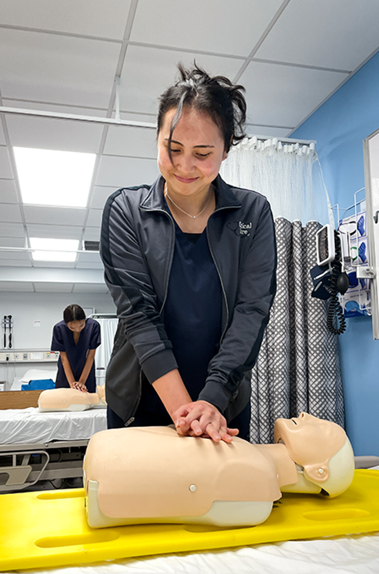 A student with her hair pulled up administers chest compressions on a manikin